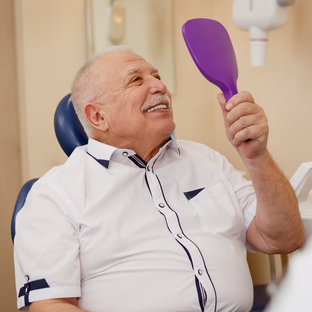 man smiling at his teeth in a handheld mirror at oxford dental